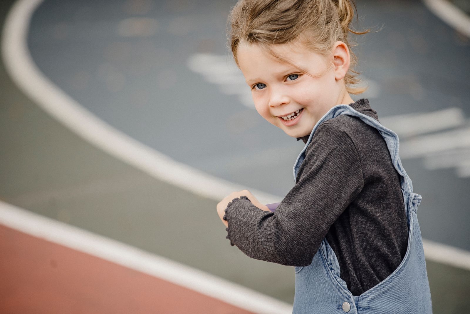 Crop happy child in casual outfit standing on sports ground and looking at camera