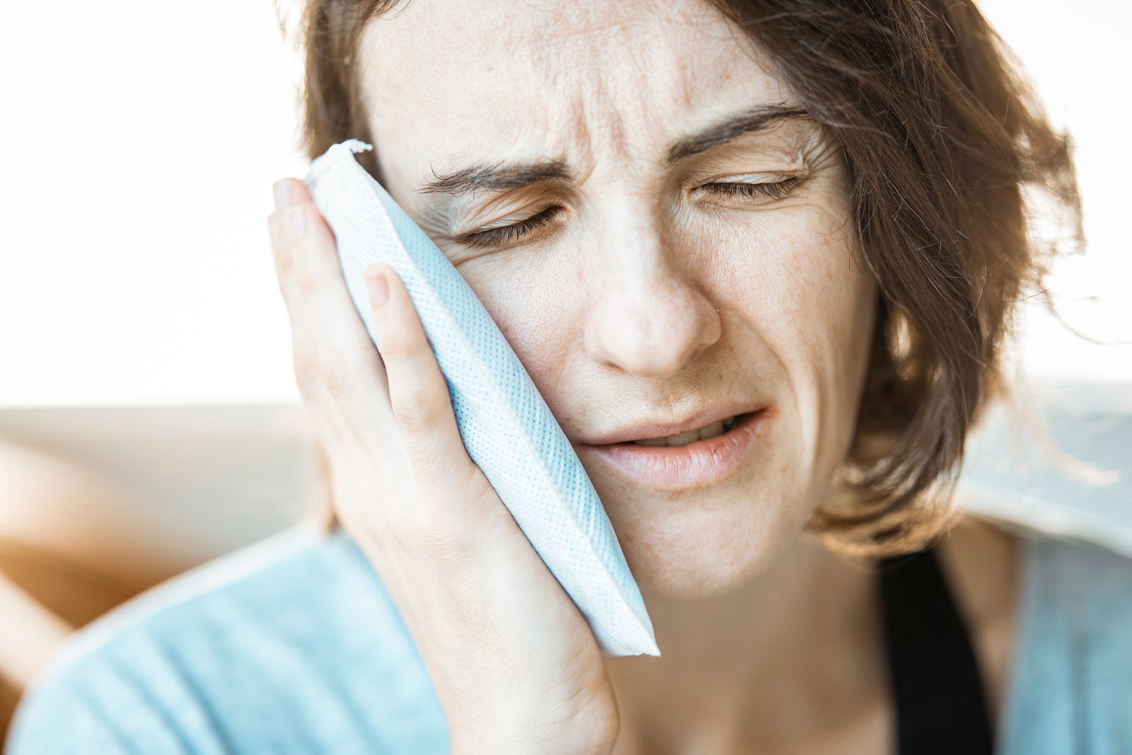 A woman in discomfort applying a cold compress to her cheek for relief from toothache pain