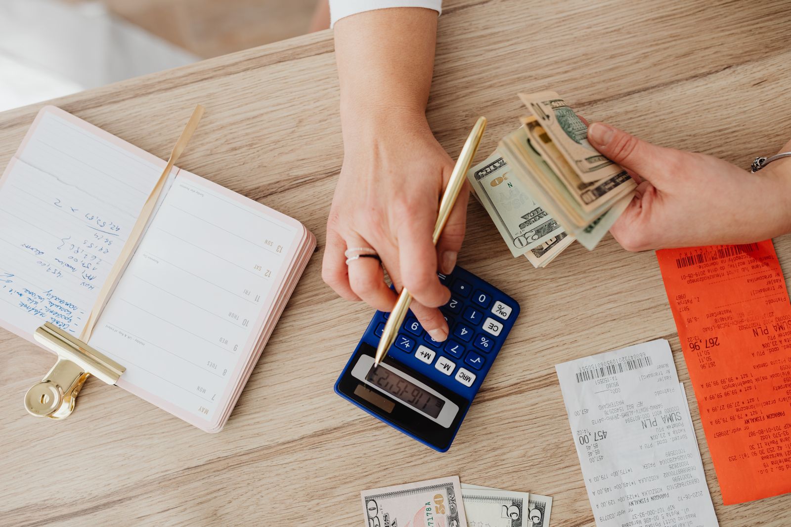 Hands managing finances with calculator, cash, and receipts on a wooden table. Ideal for budgeting concepts