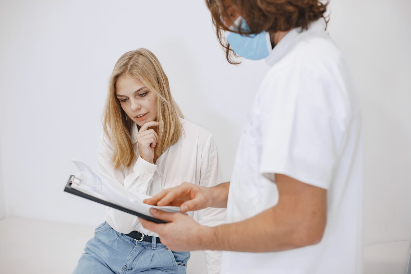 A doctor in a face mask discusses diagnosis with a patient in a clinic setting