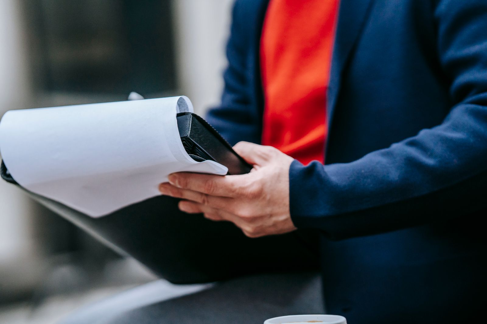 A professional adult outdoors in a suit jacket, focused on reviewing paperwork, highlighting modern business style