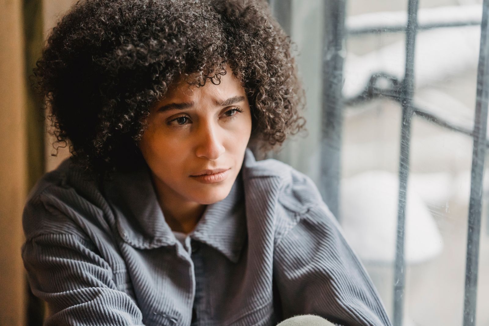 High angle of crop African American female in despair with frown face suffering from trouble sitting near window