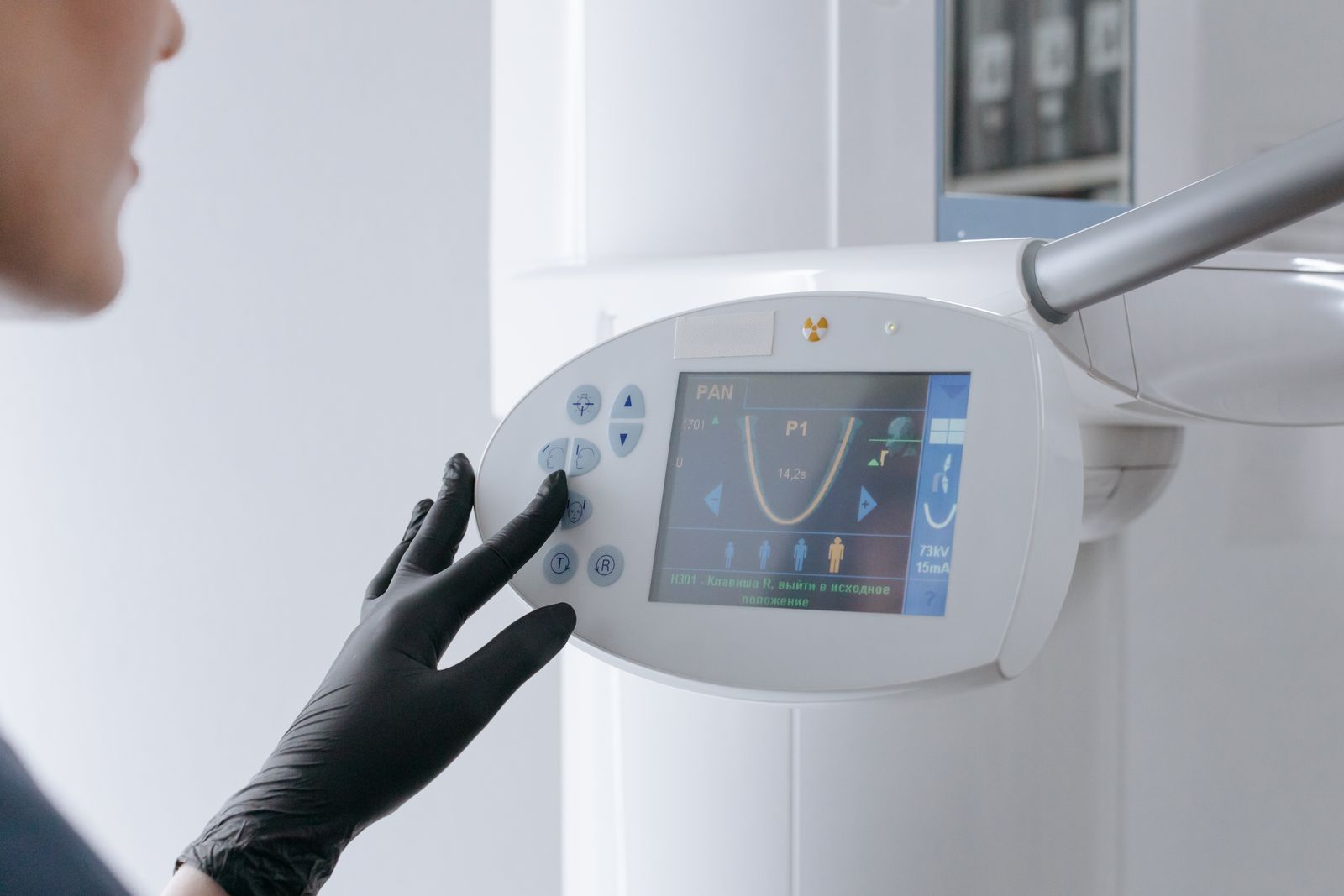 Close-up of a dental equipment screen being operated by a gloved hand in a clinic setting