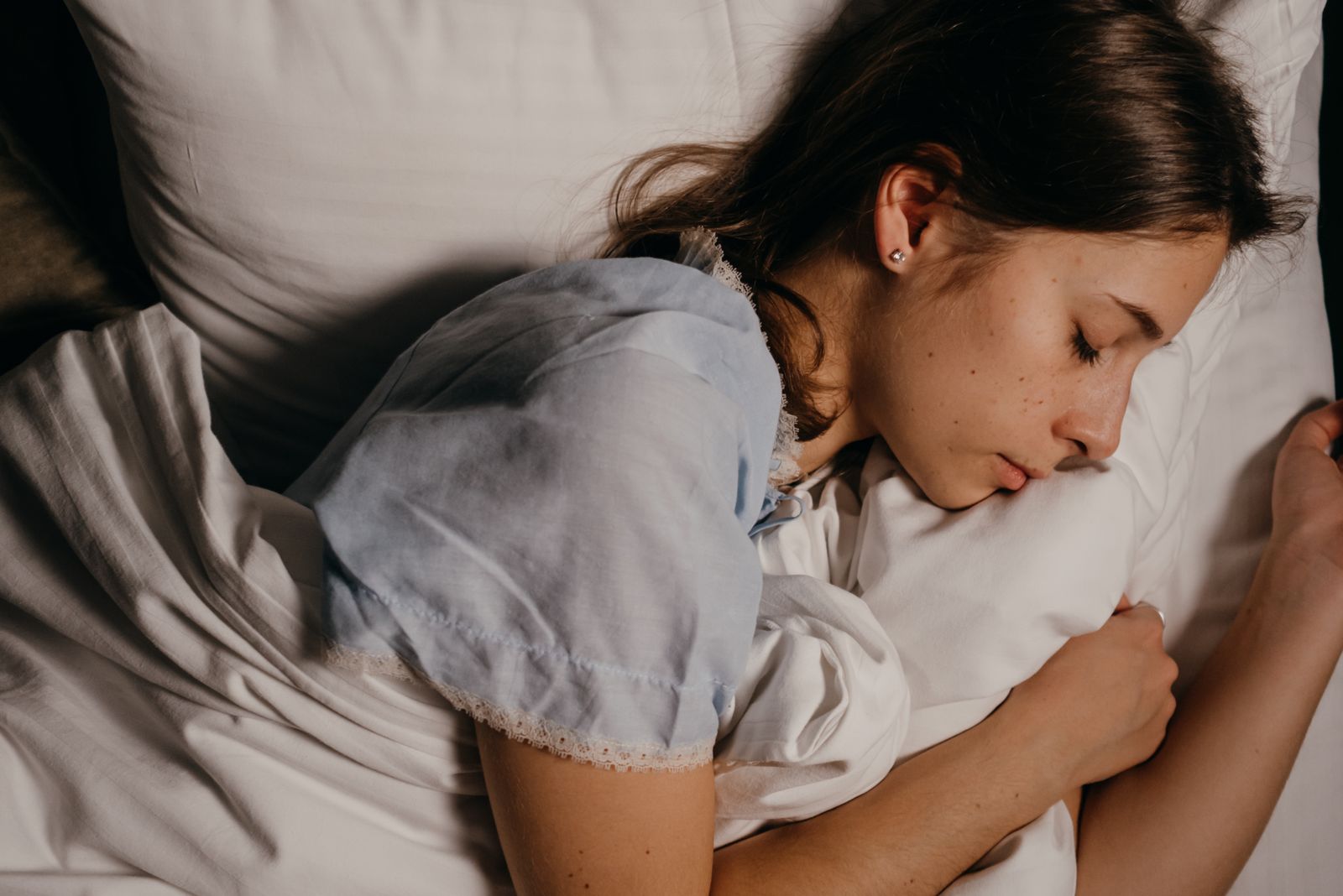 A serene young woman peacefully sleeping on a white pillow indoors at night