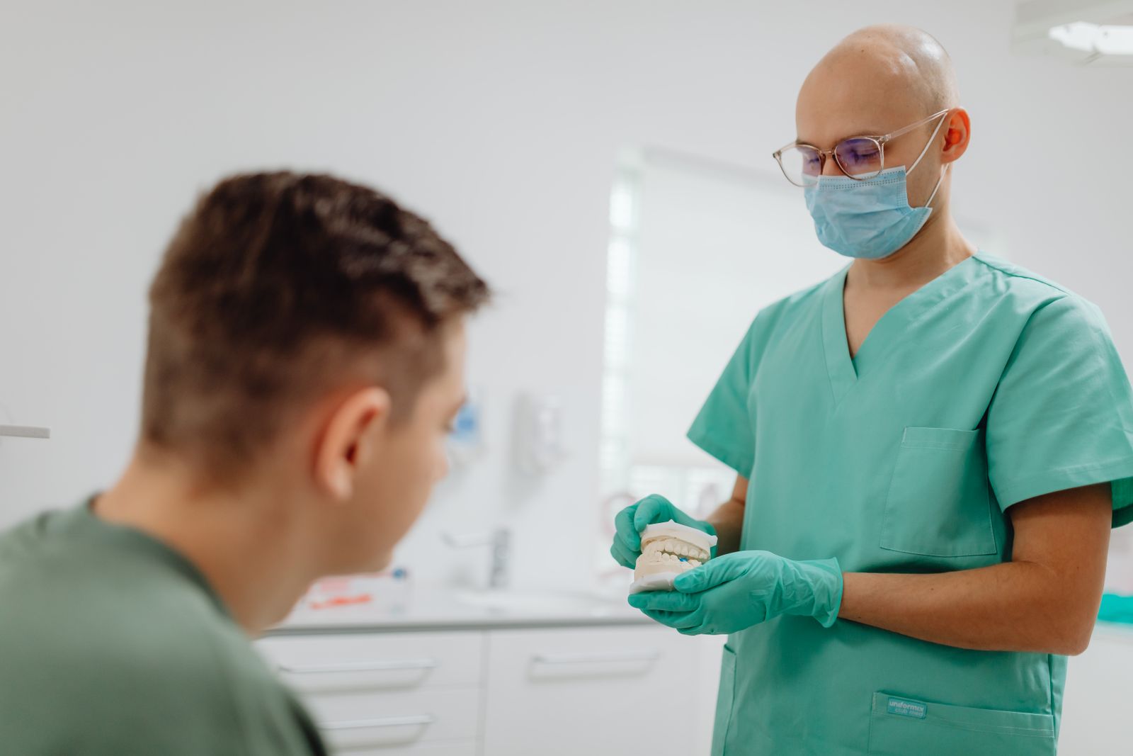 Dentist in scrubs explains dental procedure to a patient in an office setting