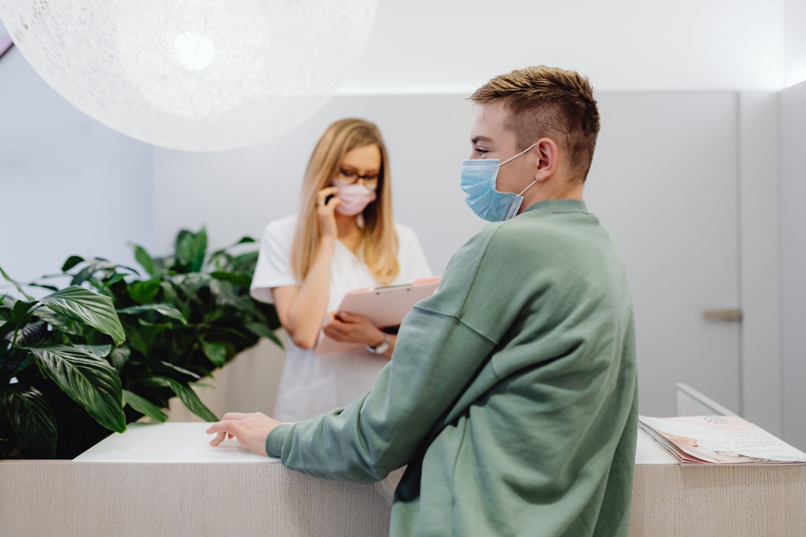 A patient and receptionist in a clinic wearing face masks, ensuring health safety