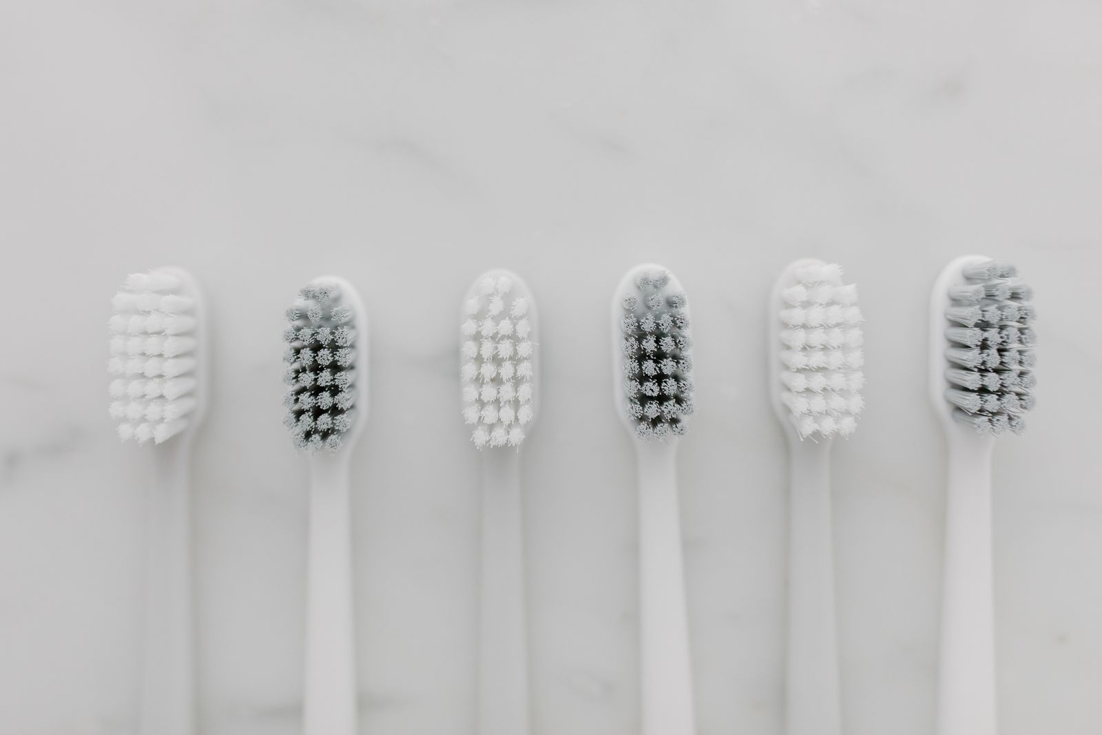 A clean, minimalist top view of six white toothbrushes on a marble surface