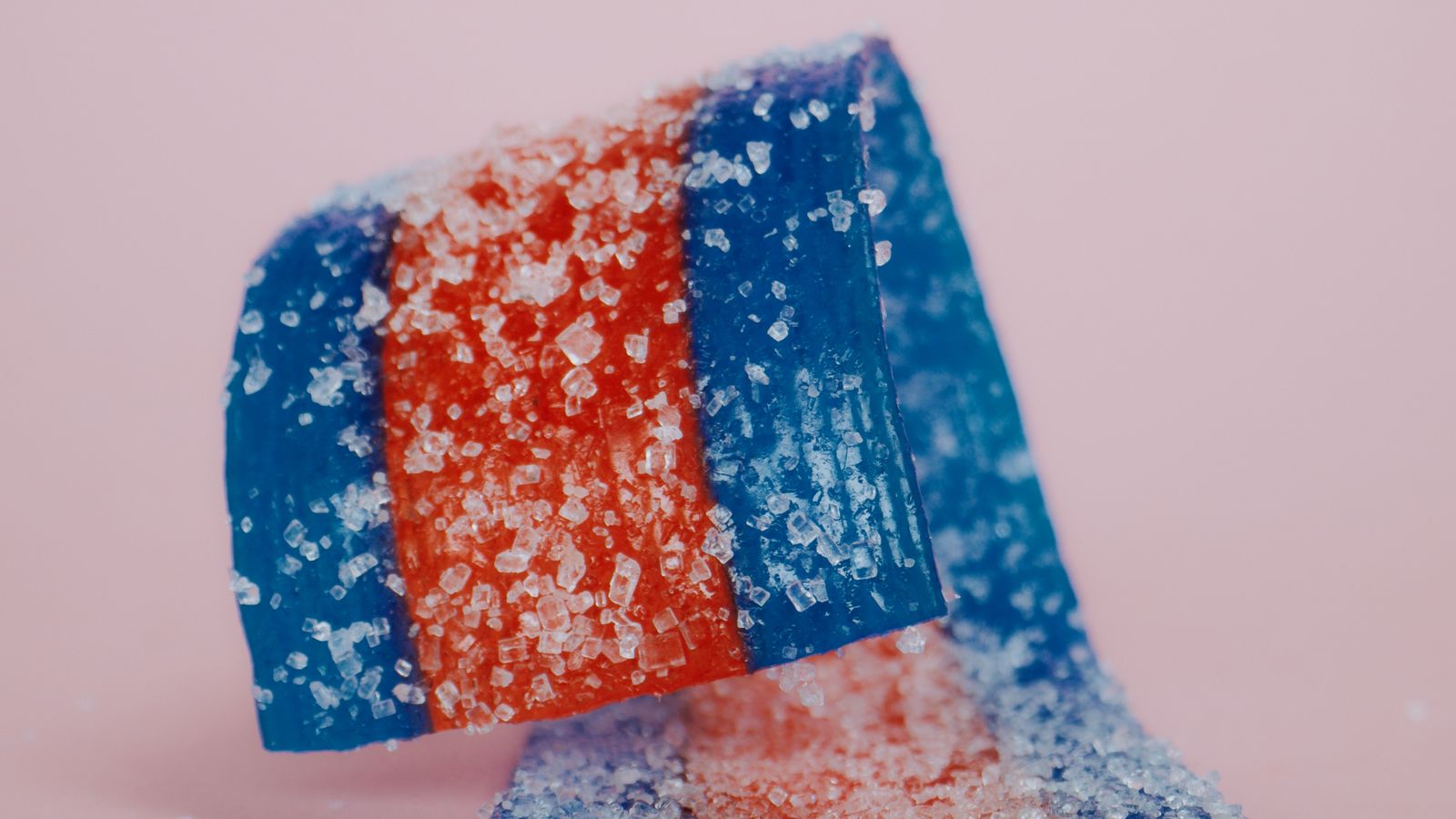 Close-up of vibrant red and blue sugared candy strips on a pink background, highlighting their texture