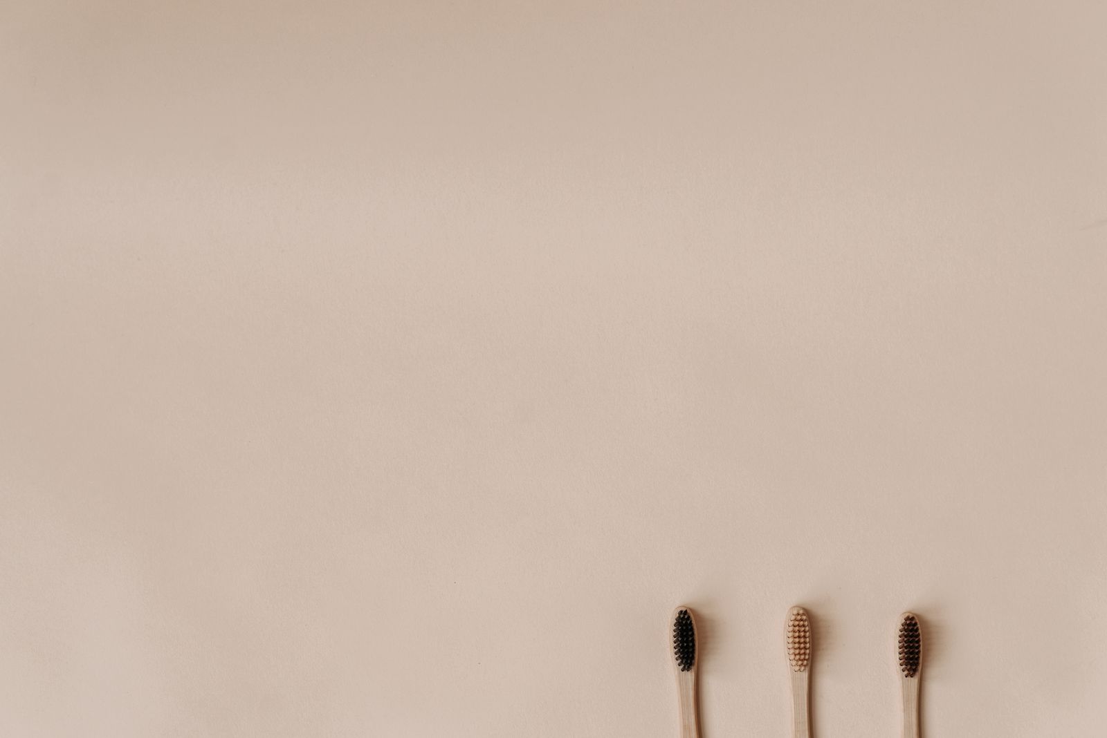 Three bamboo toothbrushes on a minimal beige background promoting eco-friendly oral care