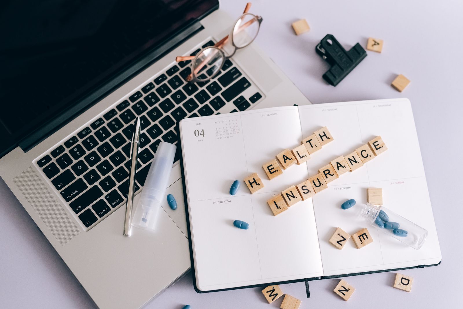 Flat lay of a laptop, notebook, and pills depicting health insurance planning