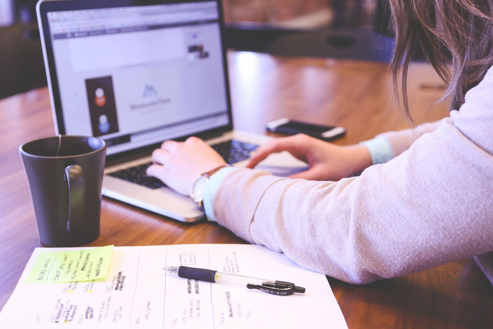 Businesswoman typing on laptop with notes and coffee on wooden desk