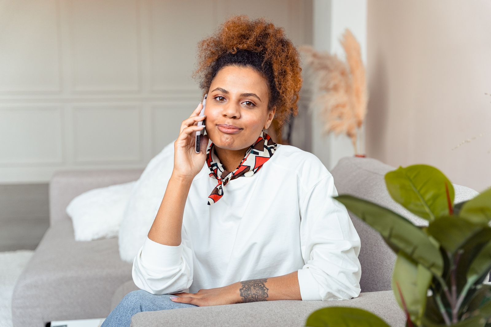 Young woman smiling while talking on the phone, sitting comfortably on a couch indoors