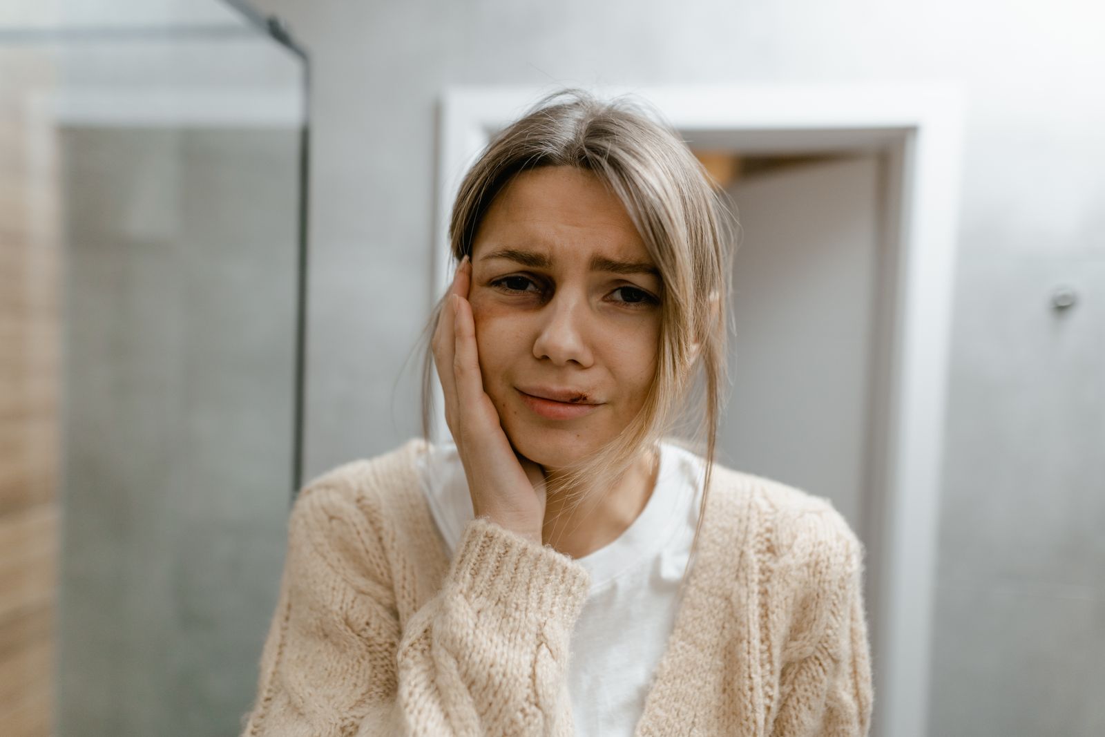 A worried woman stands indoors, touching her face, displaying signs of discomfort