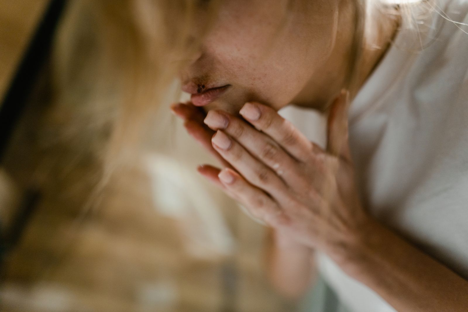 A close-up of a woman's face showing a bruise and hands touching her lips, indoors