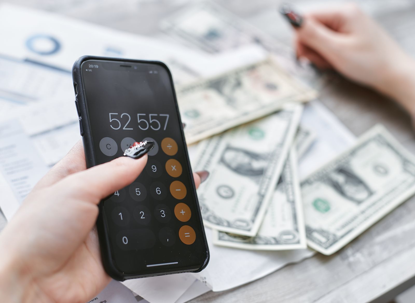 Close-up of hands using smartphone calculator next to dollar bills on table. Financial planning concept