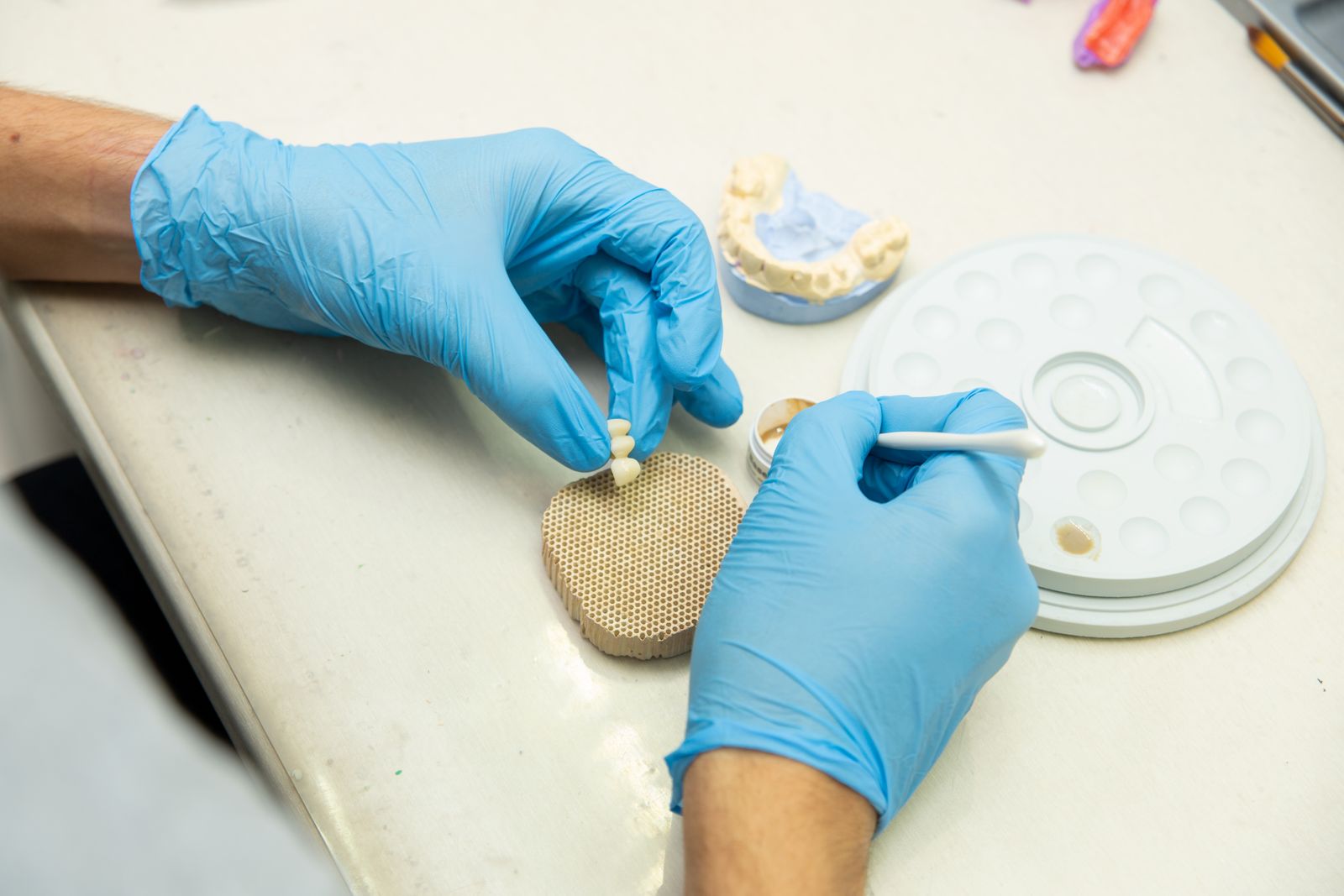 From above of crop anonymous orthodontist in latex gloves creating fake teeth for denture while sitting at table in light dental c