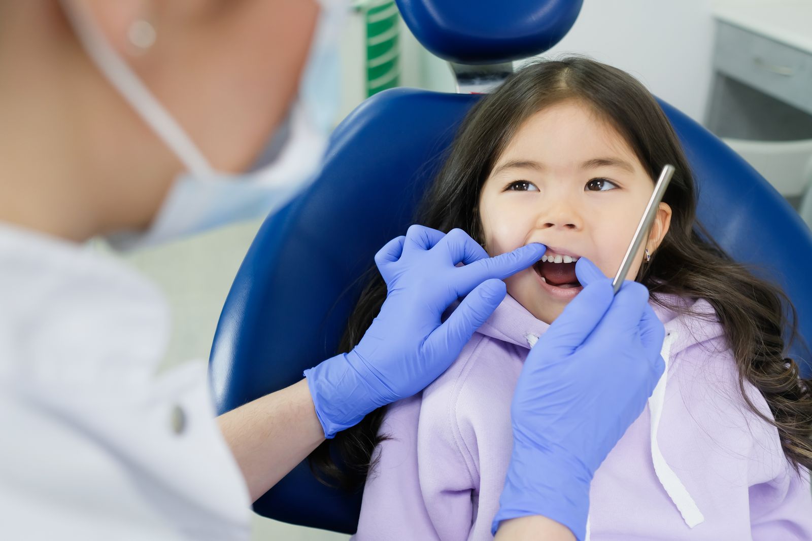 A young girl receives a dental checkup by a dentist wearing gloves in a clinic setting