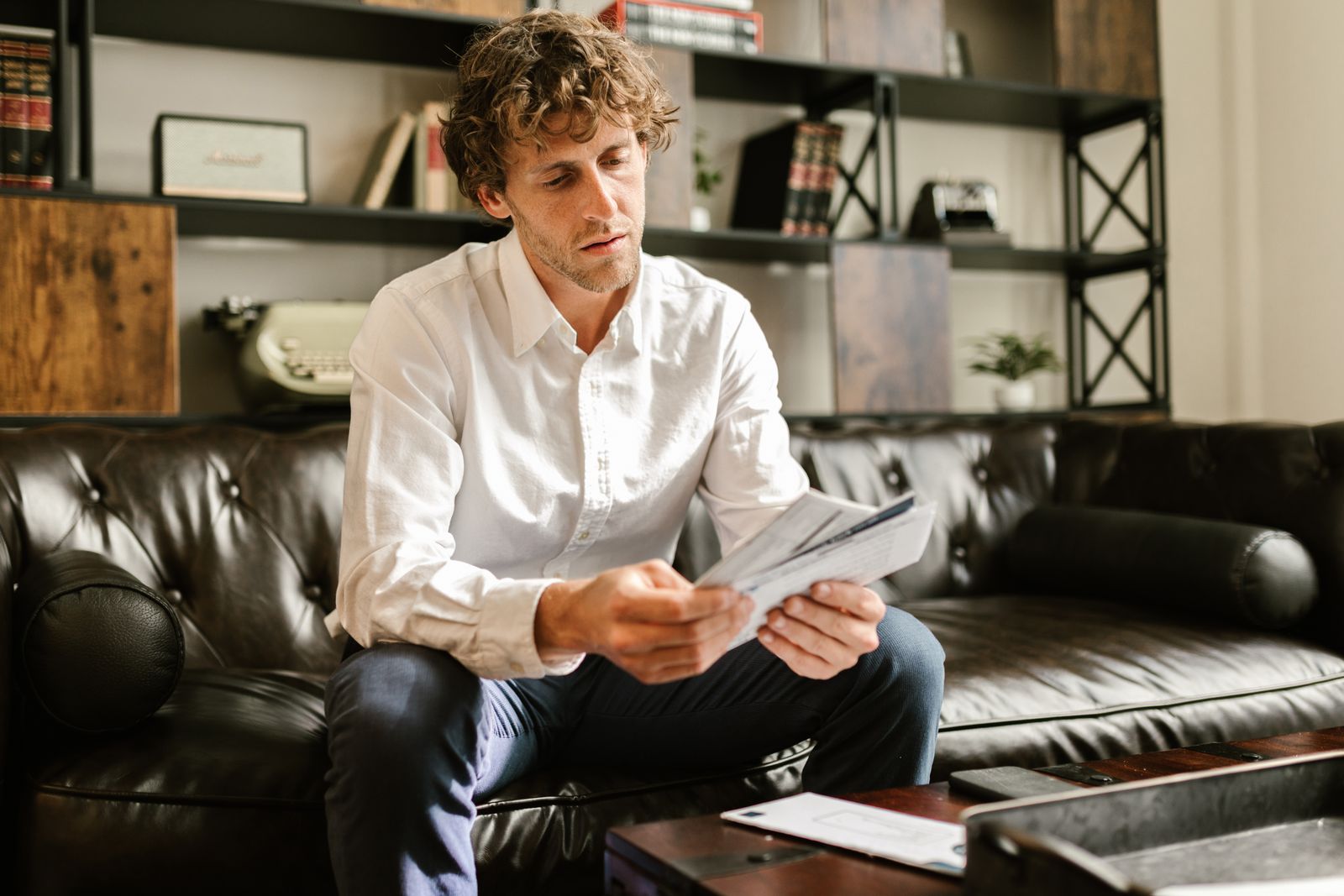 Adult man sitting on leather sofa in home office, reading documents