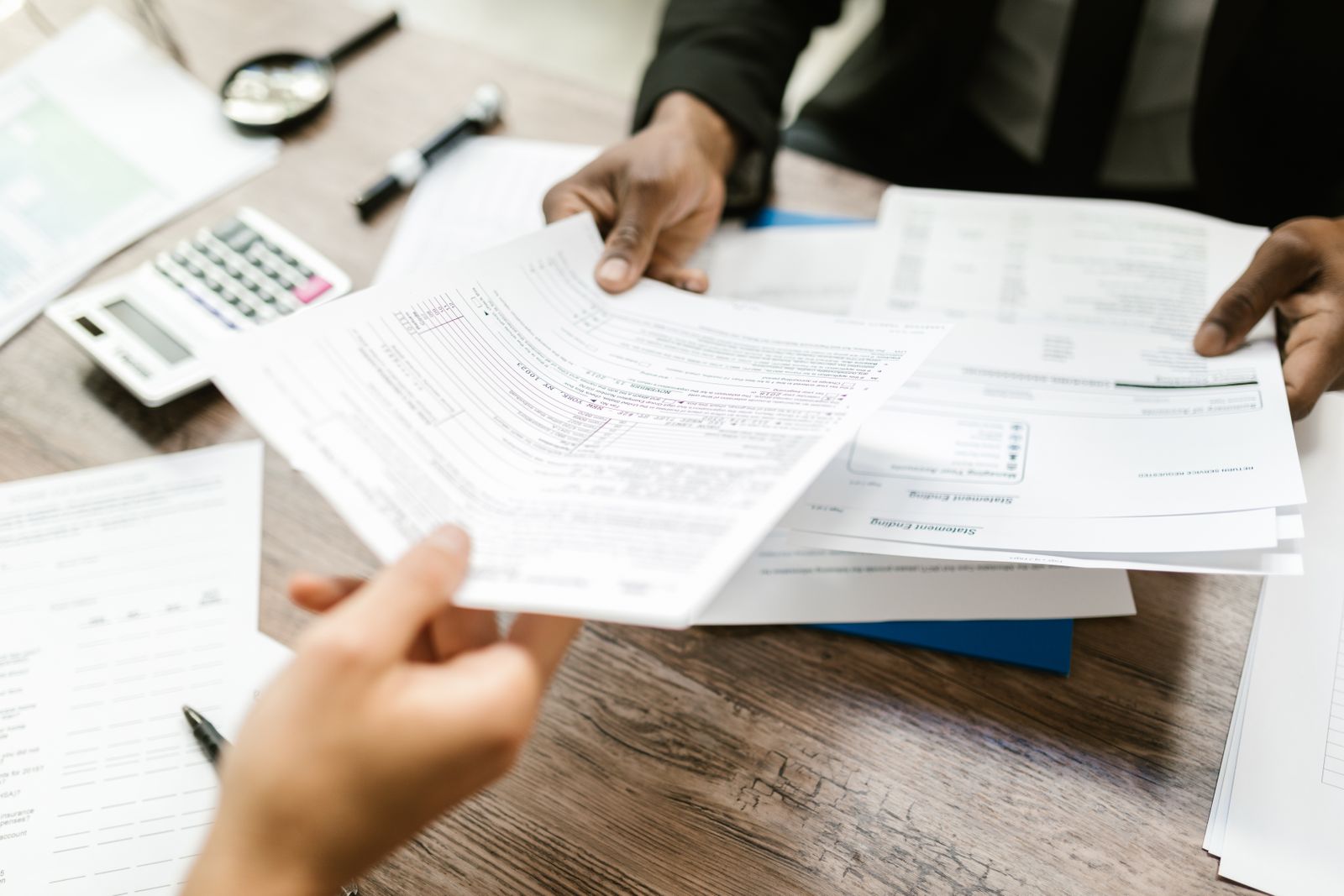 Two professionals exchanging documents in an office setting, focusing on paperwork and data analysis
