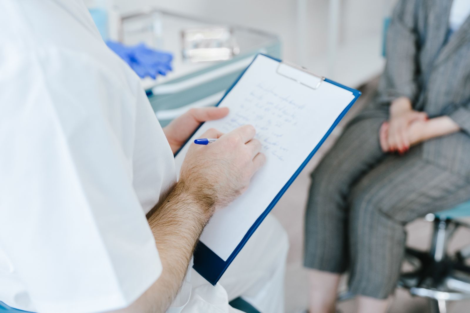 Medical professional writing patient notes on clipboard during consultation