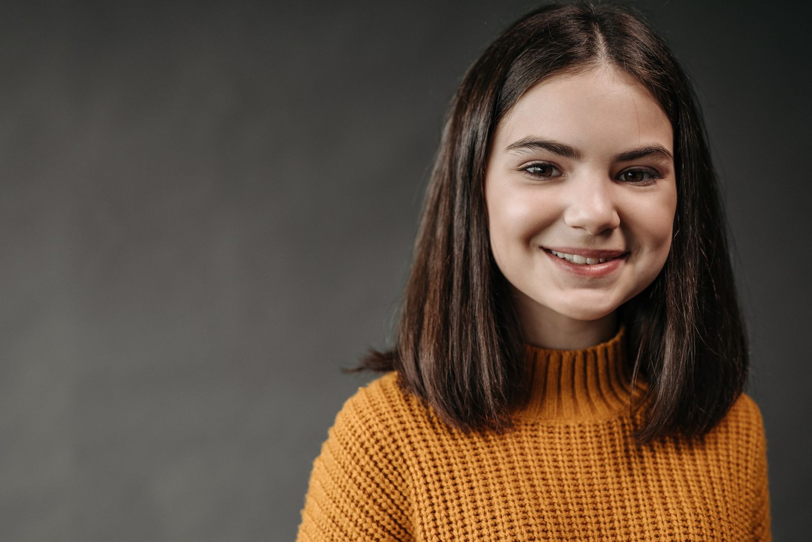 Portrait of a smiling young woman in a cozy orange knitted sweater against a neutral background