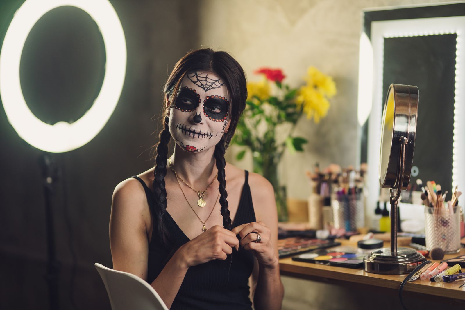 A woman with Catrina face paint prepares for Dia de los Muertos indoors