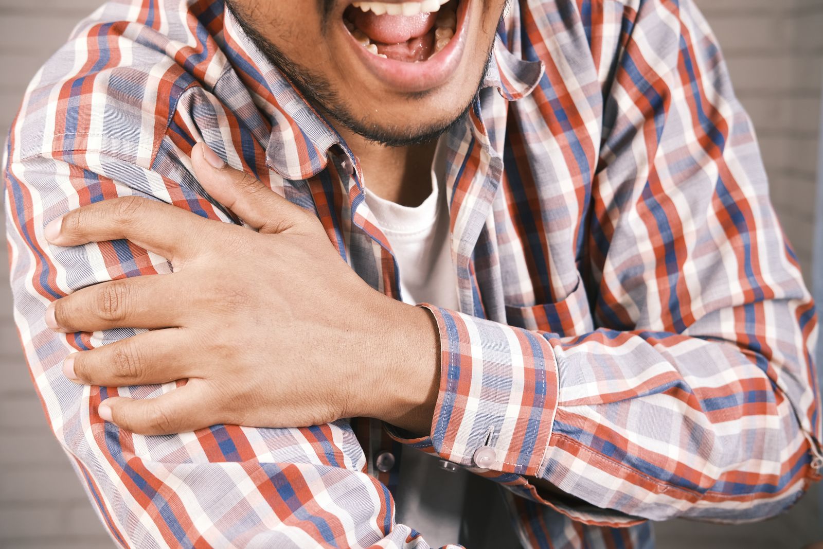 Close-up of a man in plaid shirt experiencing shoulder pain, grasping his arm