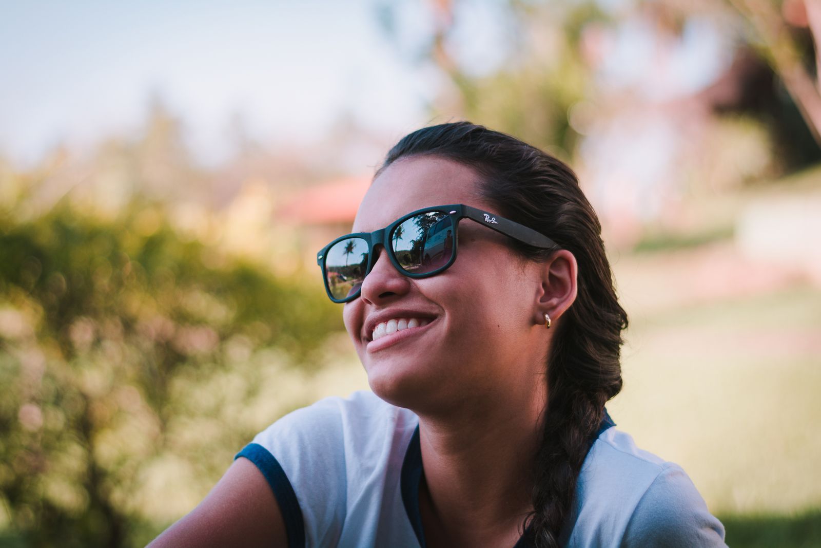 Young woman smiling outdoors wearing sunglasses, embracing a carefree summer vibe