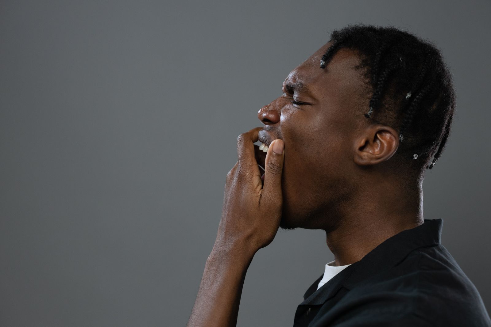 Close-up side view of a black man yawning against a neutral background. Minimalist and candid