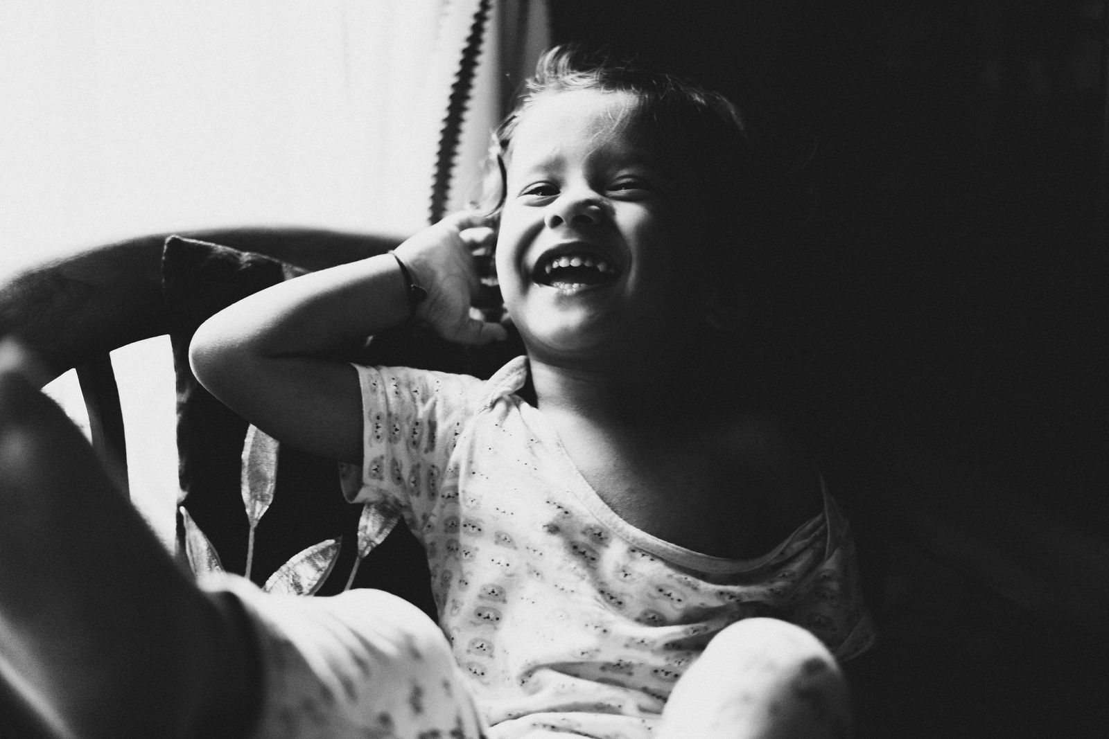 Smiling child in black and white, capturing carefree joy near a sunny window